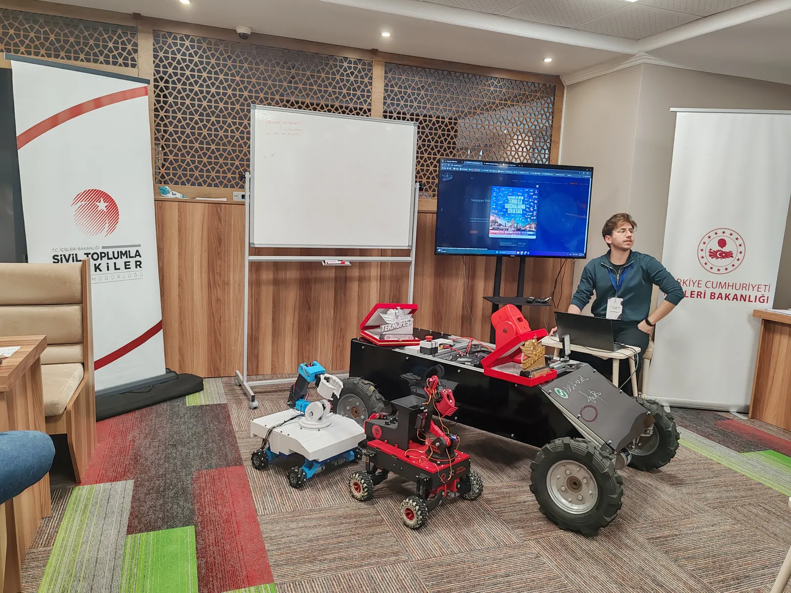 Tematik Kış Kampı mekatronik oturumu: yerde tekerlekli robotlar, arkada ekranın yanında eğitmen