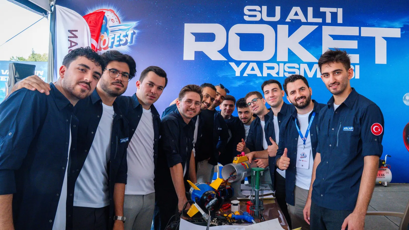 Su Altı Roket takımı yarışma afişinin önünde, masada roket