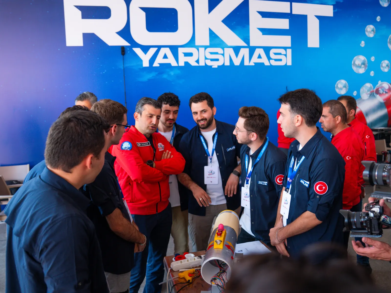Takım üyeleri ve ziyaretçiler masadaki su altı roketinin çevresinde