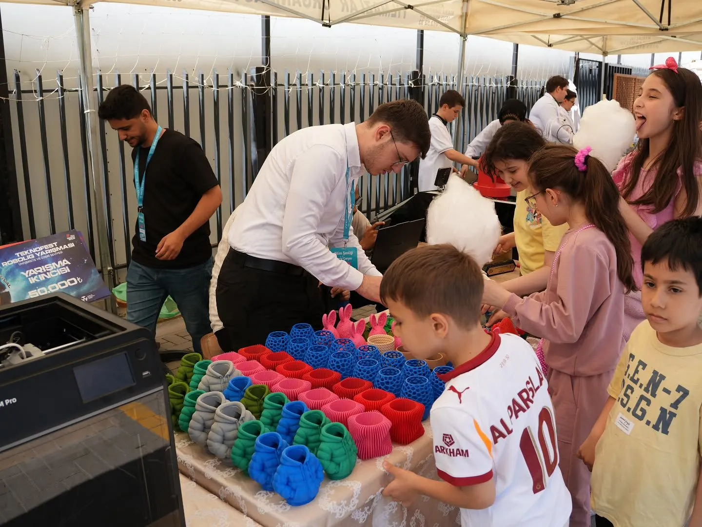 Standda çocuklar masadaki renkli 3D baskı parçalarına bakıyor