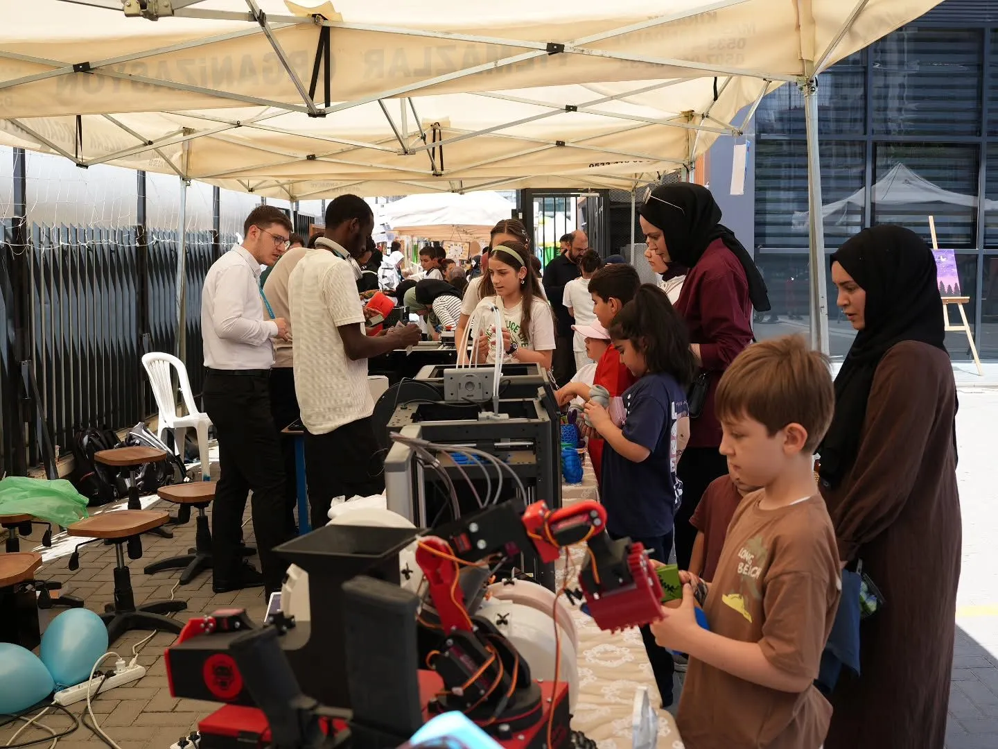 Standda robot kol ve 3D yazıcılar, ziyaretçiler izliyor