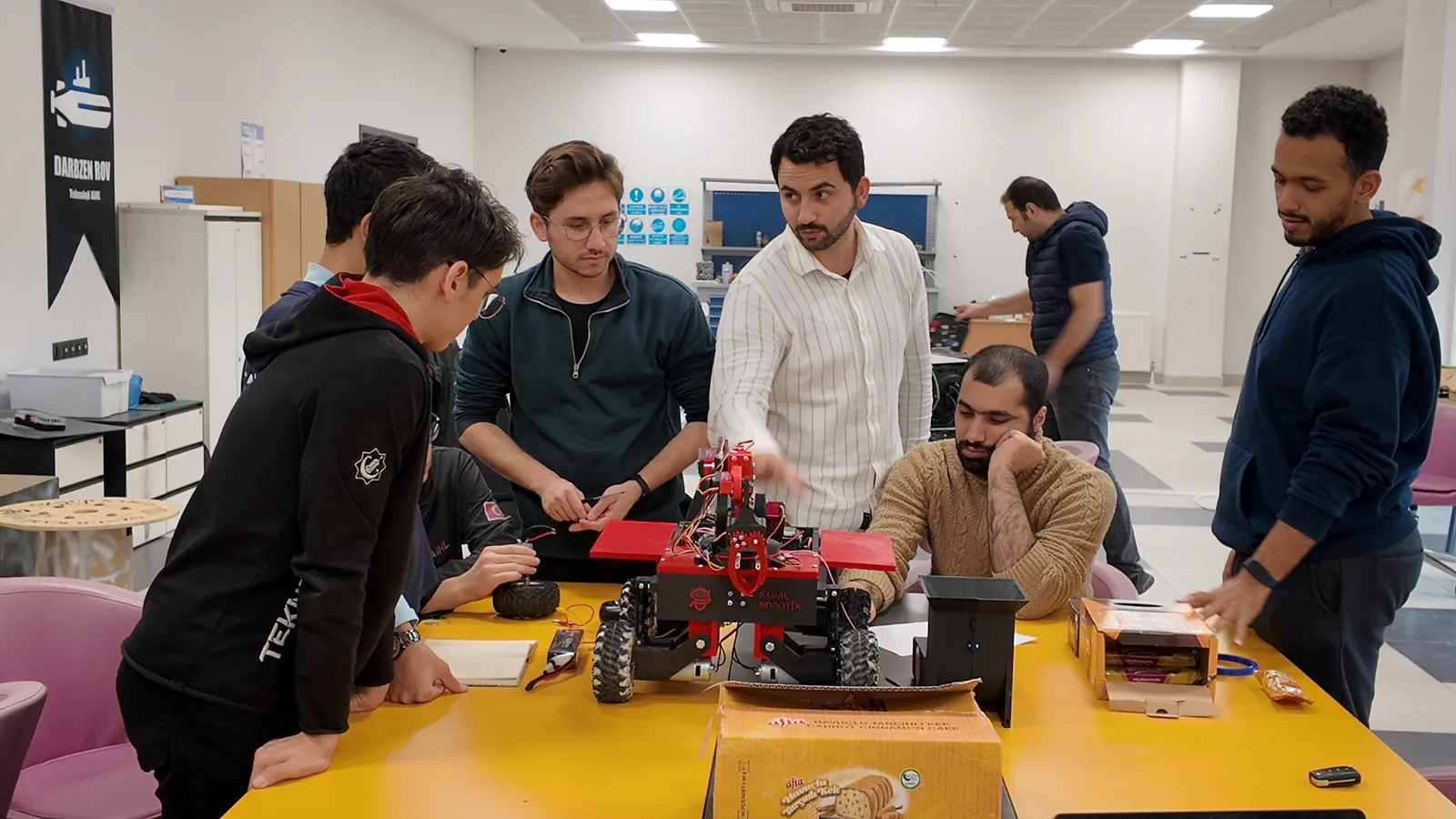 Öğrenciler masadaki kırmızı robot aracın başında