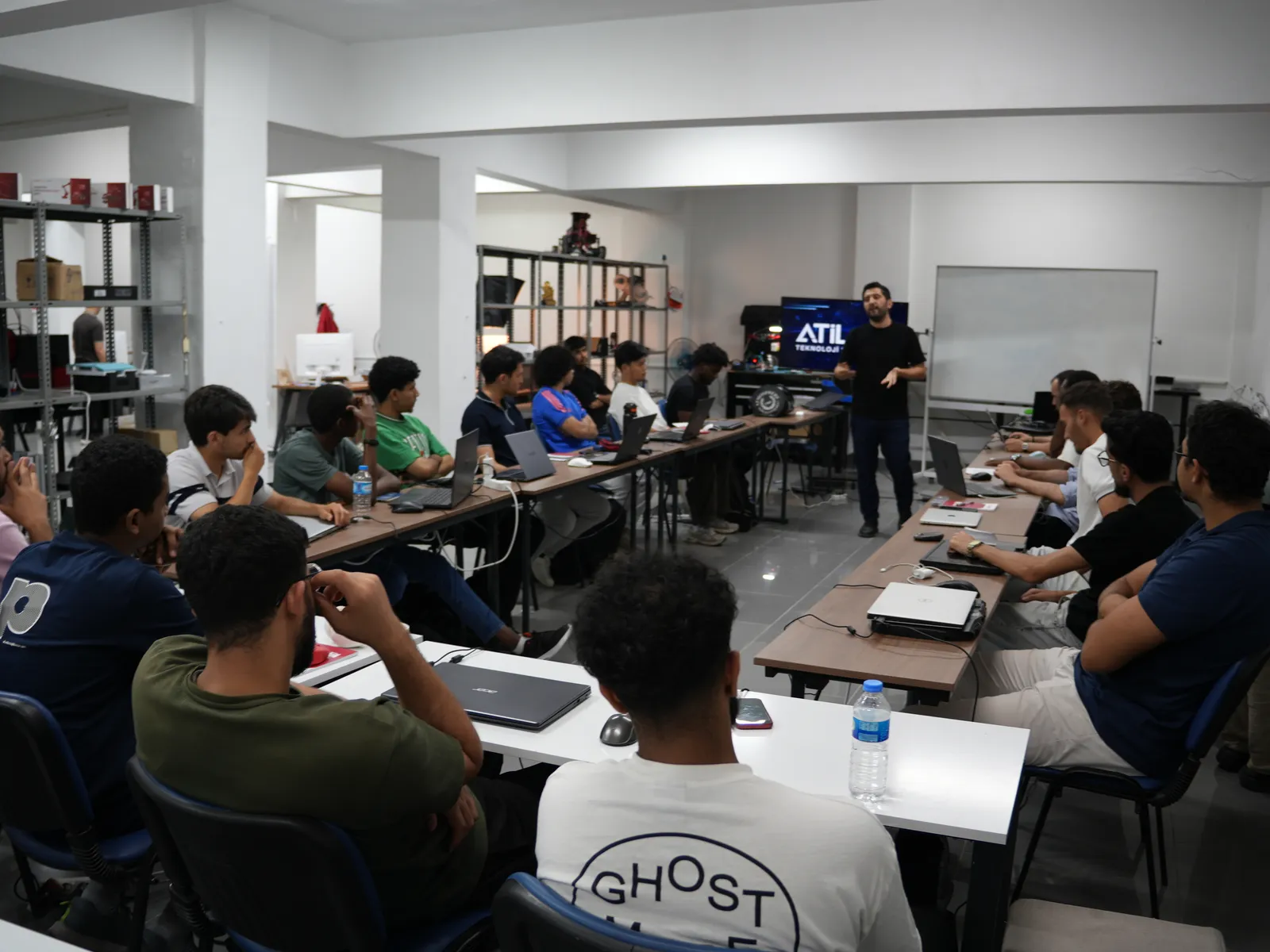 ATİLAB laboratuvarında dizüstü bilgisayarlarıyla oturan stajyerler, arkada eğitmen